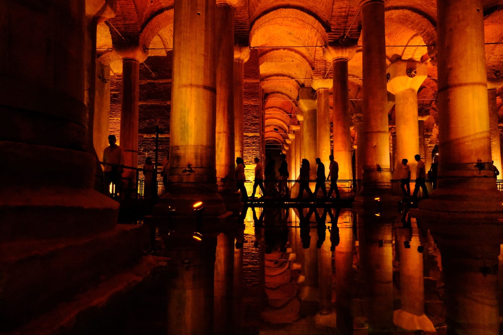 Visiteurs longeant les colonnes illuminées de la Citerne Basilique en nocturne.
