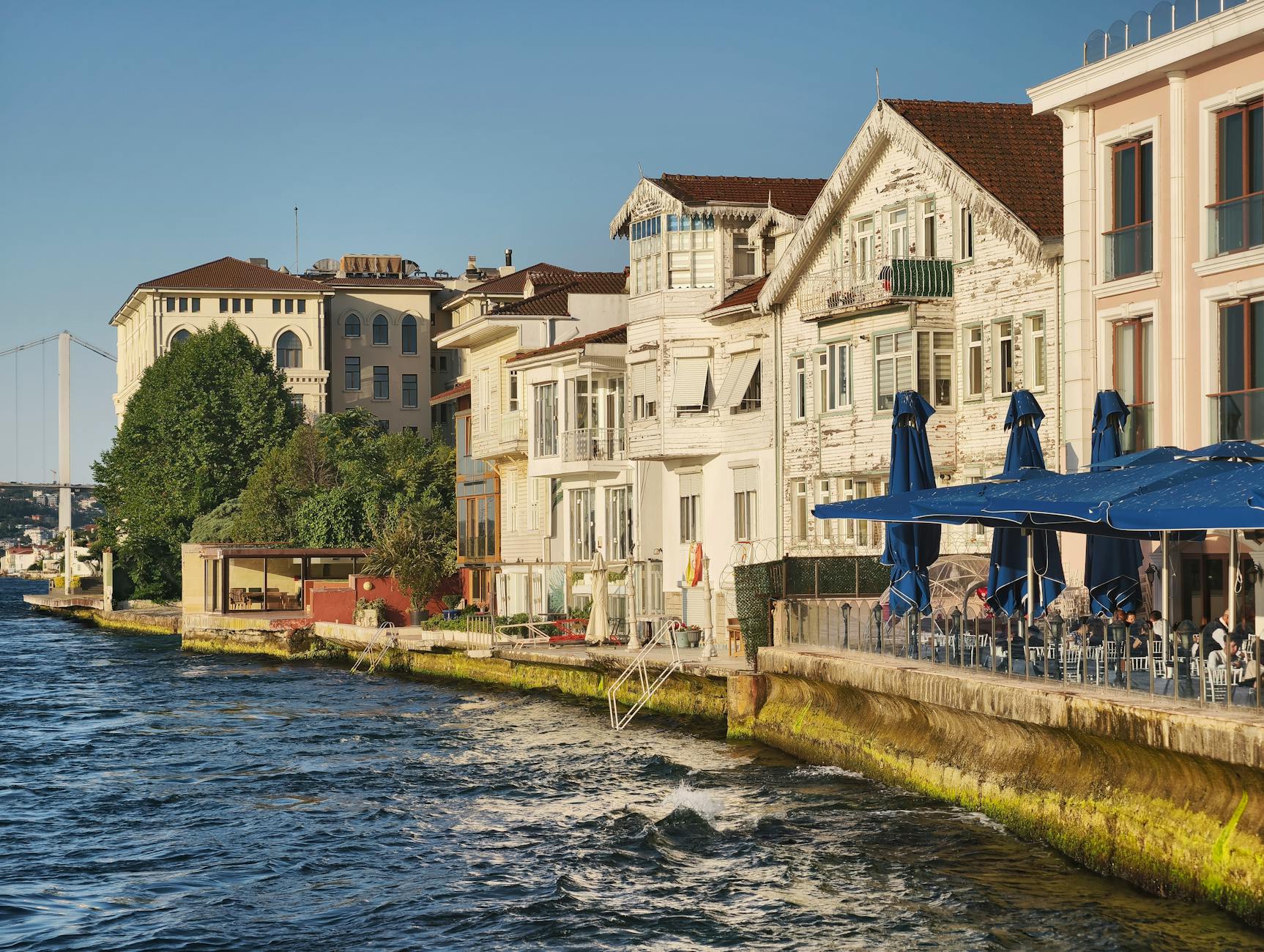 Vue des traditionnelles maisons en bois (Yalis) du Bosphore à Istanbul, bordant l'eau avec des terrasses de restaurant et le pont en arrière-plan.