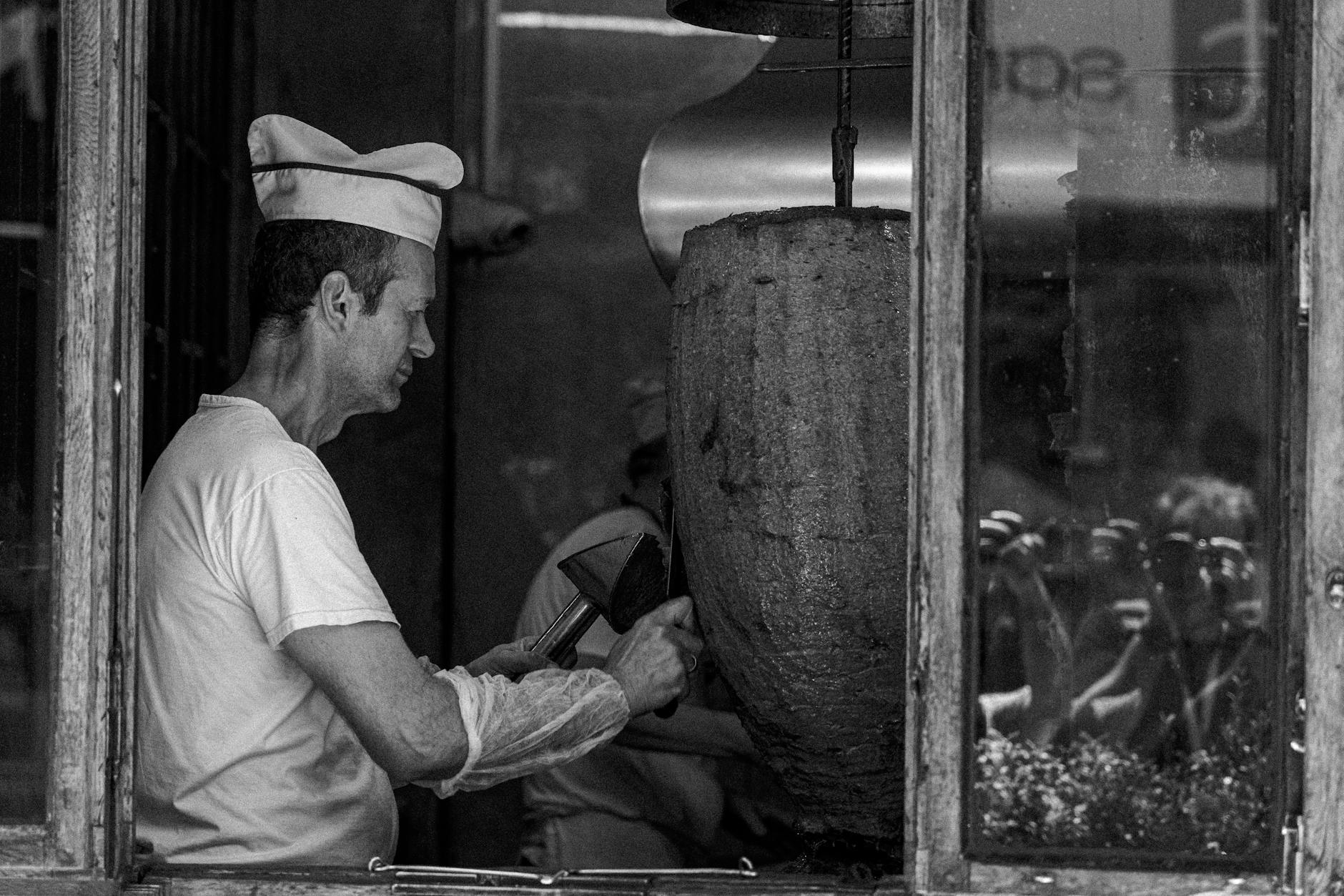 Artisan tranchant avec précision une imposante broche de viande de döner vertical.