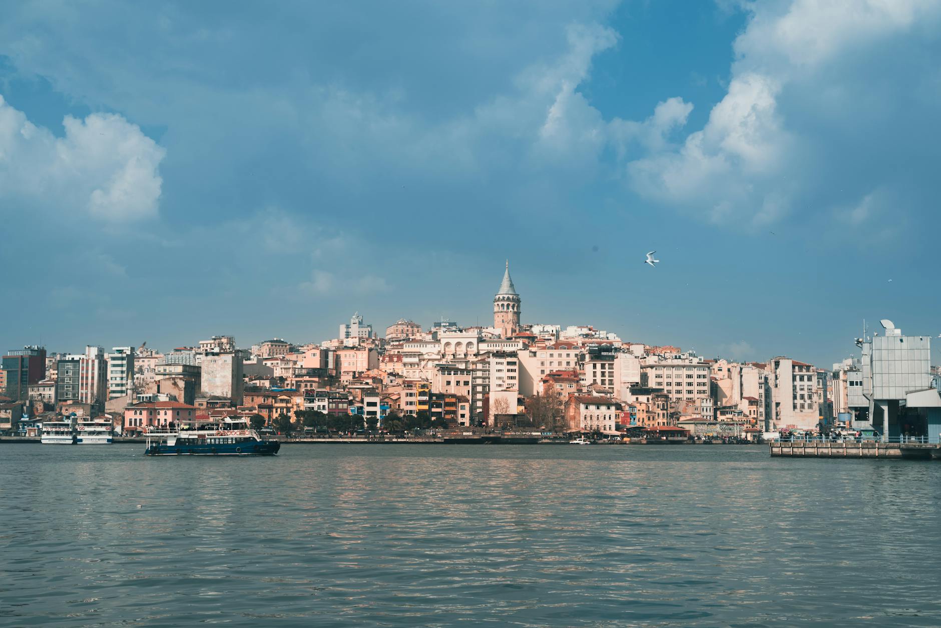 Vue panoramique de la ligne d'horizon de Beyoğlu, Istanbul, avec la Tour de Galata dominant les bâtiments colorés, vue depuis l'eau avec un ferry au premier plan.