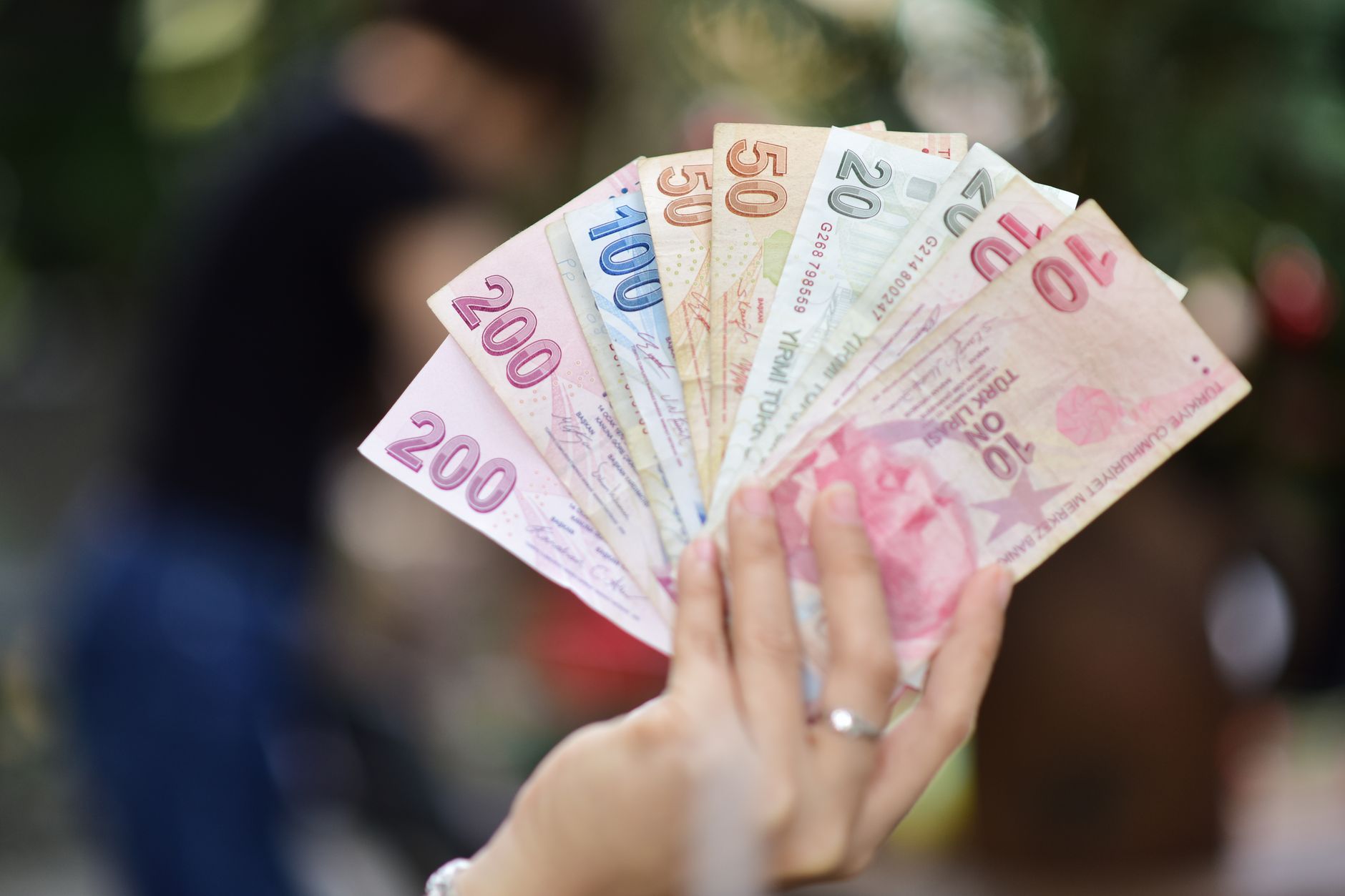 Mains tenant un éventail de billets récents en livres turques.