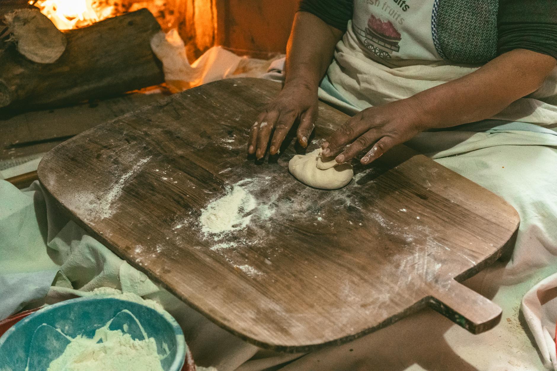 Artisane préparant de la pâte à pain sur une grande planche en bois.