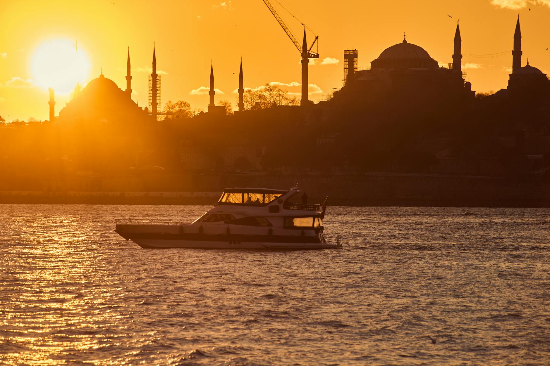Yacht privé naviguant sur le Bosphore au coucher du soleil, silhouette des mosquées historiques d'Istanbul à l'arrière-plan.