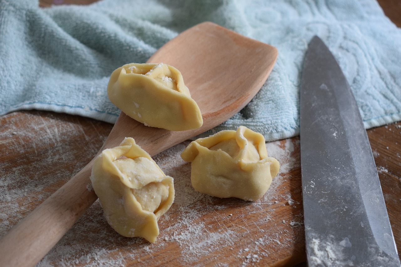 Trois manti traditionnels crus disposés sur une planche en bois.