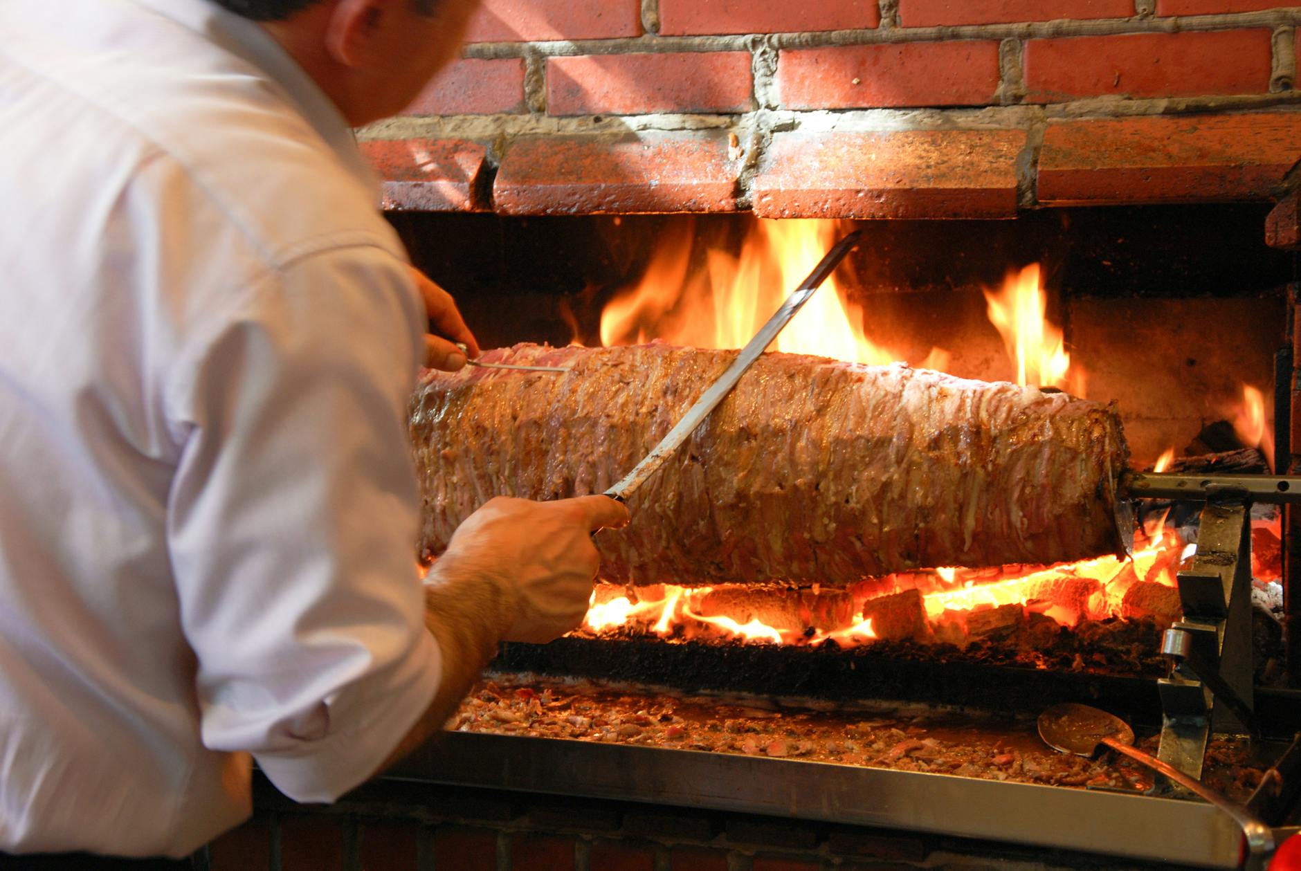 Chef préparant un Cağ Kebab traditionnel sur une broche horizontale au feu de bois.
