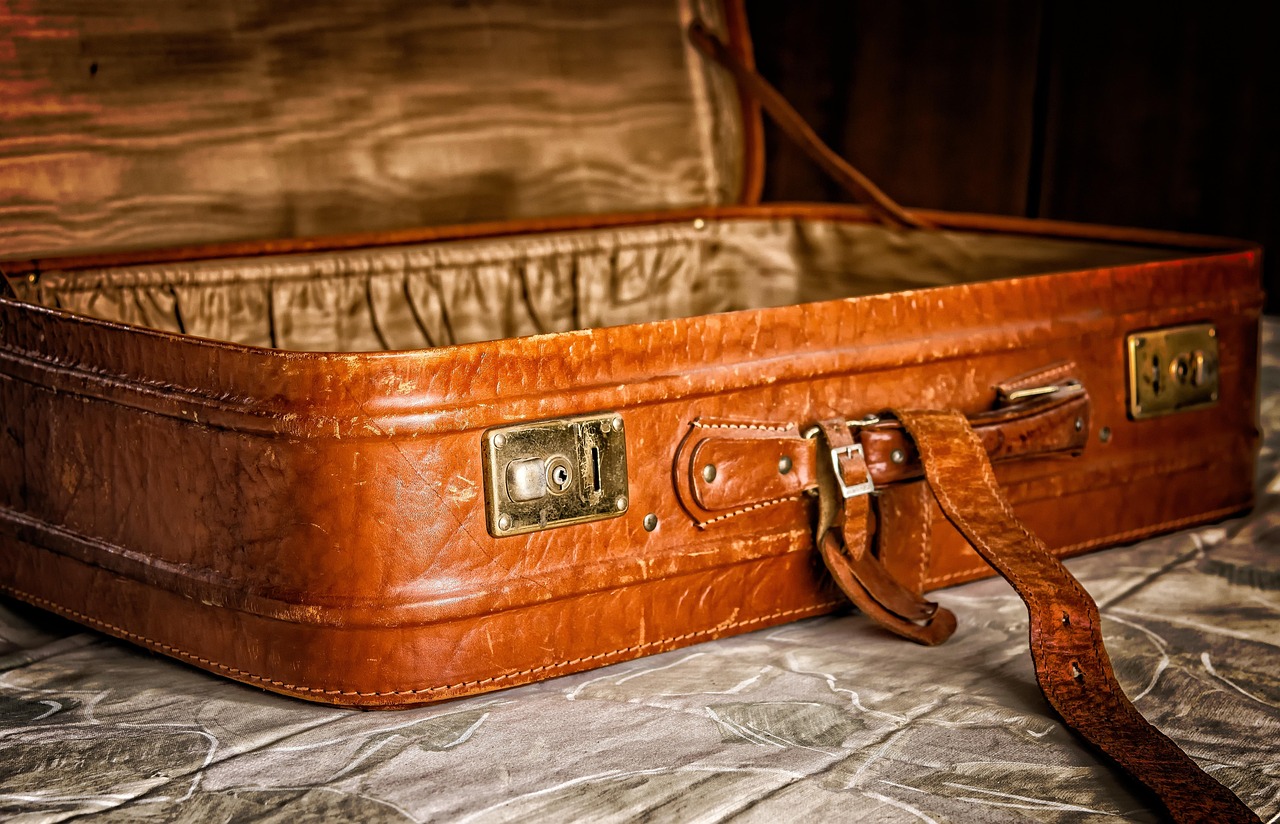 Une valise ancienne en cuir marron ouverte posée sur un lit.